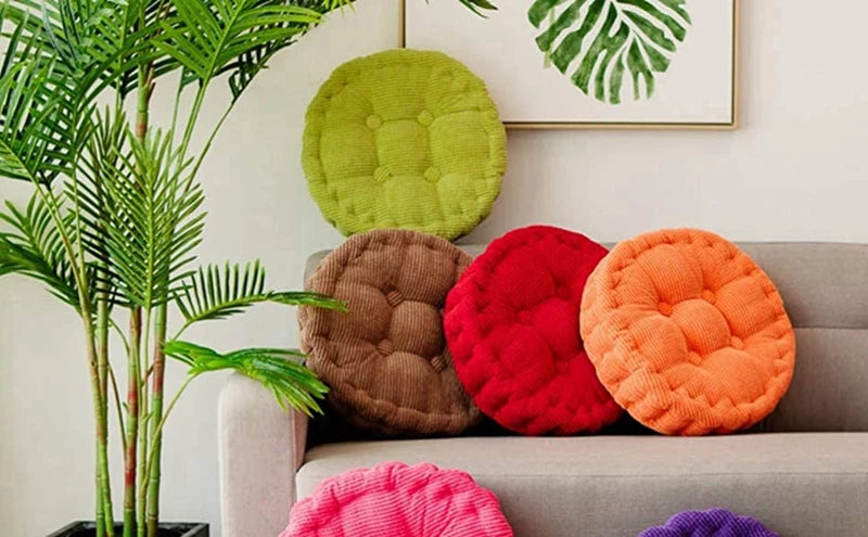 A collection of colorful thick corduroy floor cushions in green, brown, red, orange, and pink resting on a sofa.