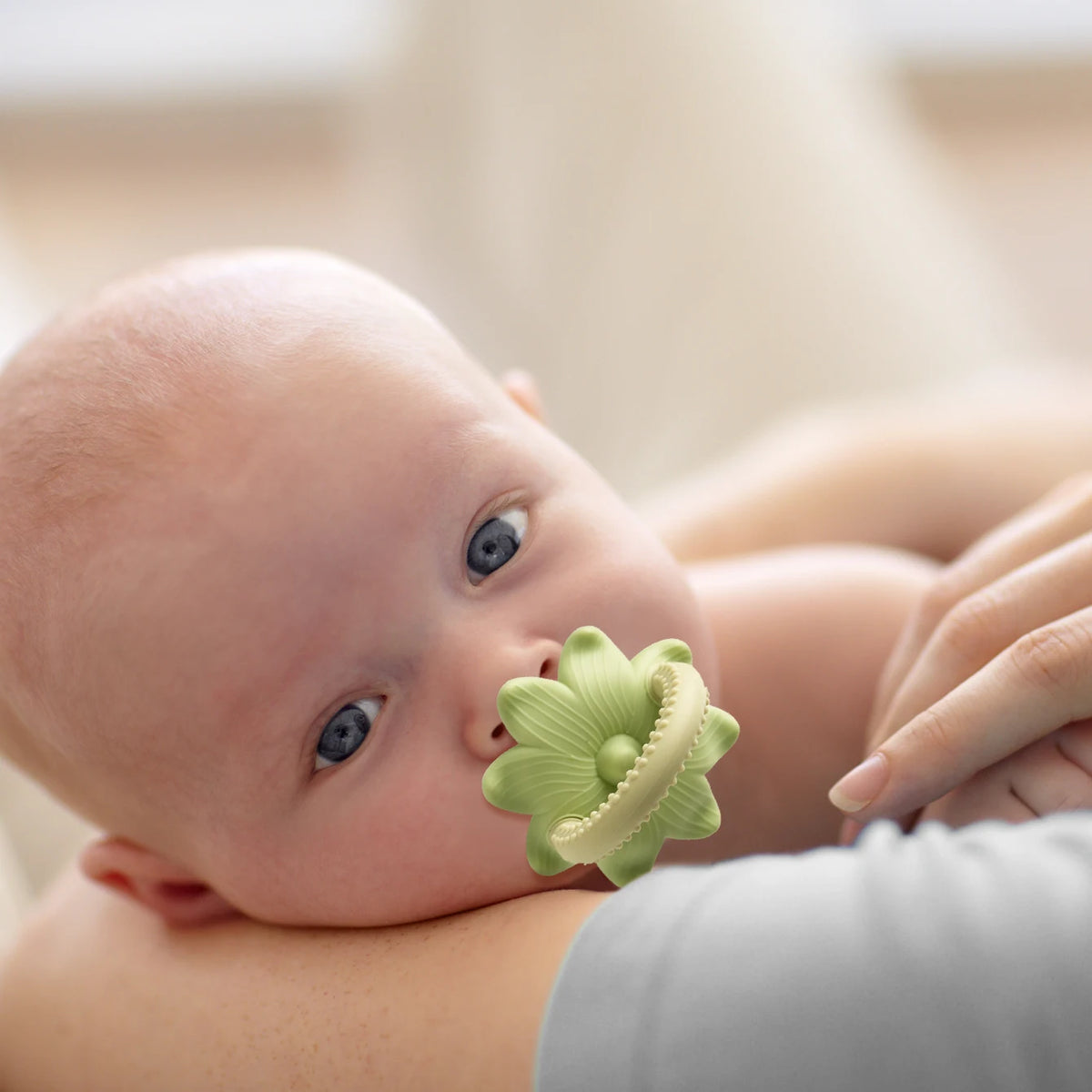 A close-up of a baby's face being gently touched by a silicone baby teether toy shaped like a flower and grape.