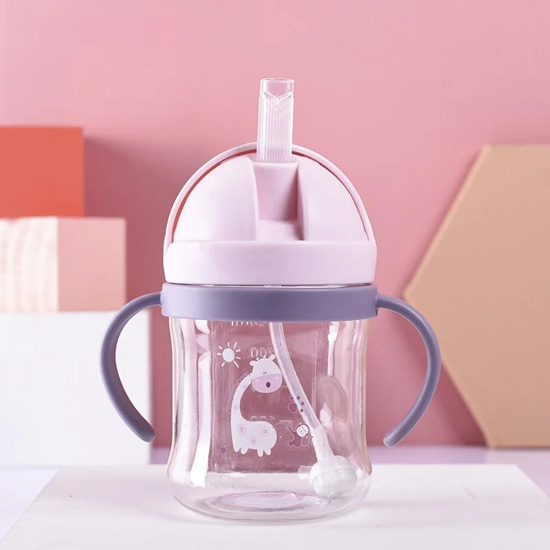 A clear glass straw cup with a pink lid and handles is shown against a light background.