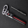 A silver key fob with a black protective cover and a metal tool is displayed on a dark surface.