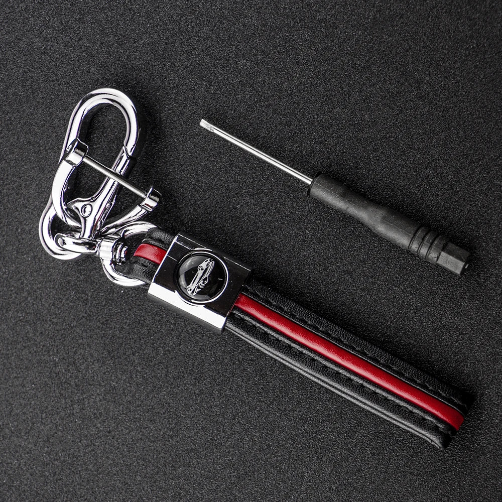 A silver key fob with a black protective cover and a metal tool is displayed on a dark surface.