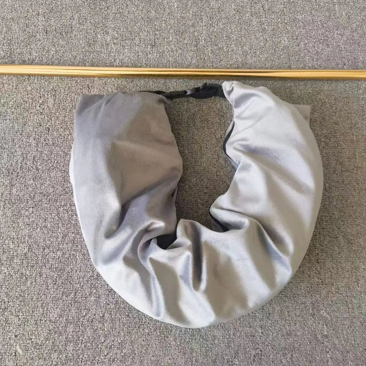 A gray self-filling travel pillowcase organizer with a black strap is shown lying on a gray fabric surface.