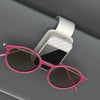 A pair of pink-framed sunglasses resting on a white magnetic glasses holder.