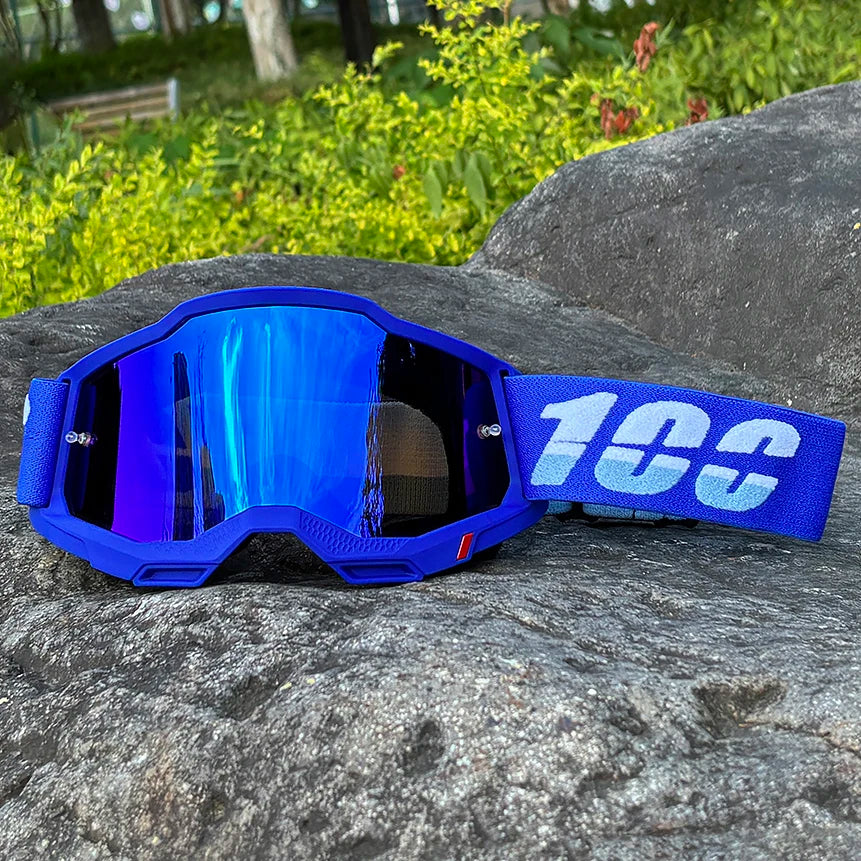 Blue motocross goggles with a blue strap resting on a gray rock outdoors.