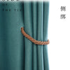 A close-up of a teal curtain fabric with a natural rope tieback in the center.