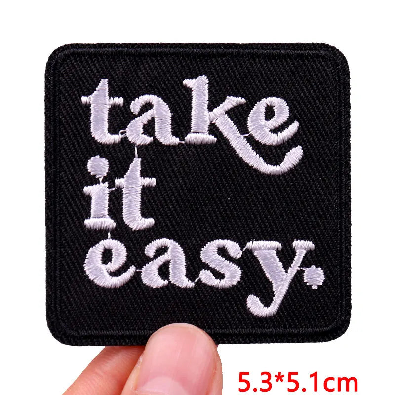 Black embroidered iron-on letter patch with white text that reads take it it easy