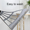 A silicone squeegee broom with a long adjustable handle is shown being washed under running water.