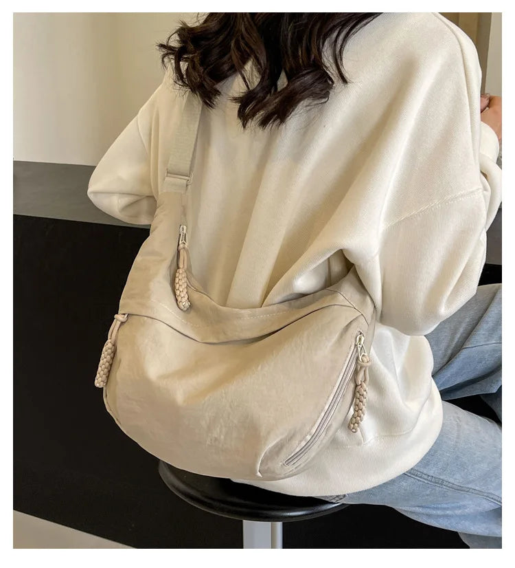 A person is wearing a beige lightweight nylon crossbody bag with an adjustable strap under a cream-colored sweatshirt.
