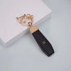 Gold-toned key fob cover with a leather strap and a decorative gold chain, resting on a white surface.