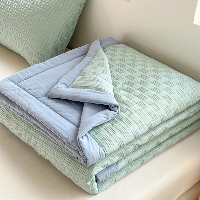 A light green waffle-weave quilt folded on a bed, featuring pale blue and sage green tones.