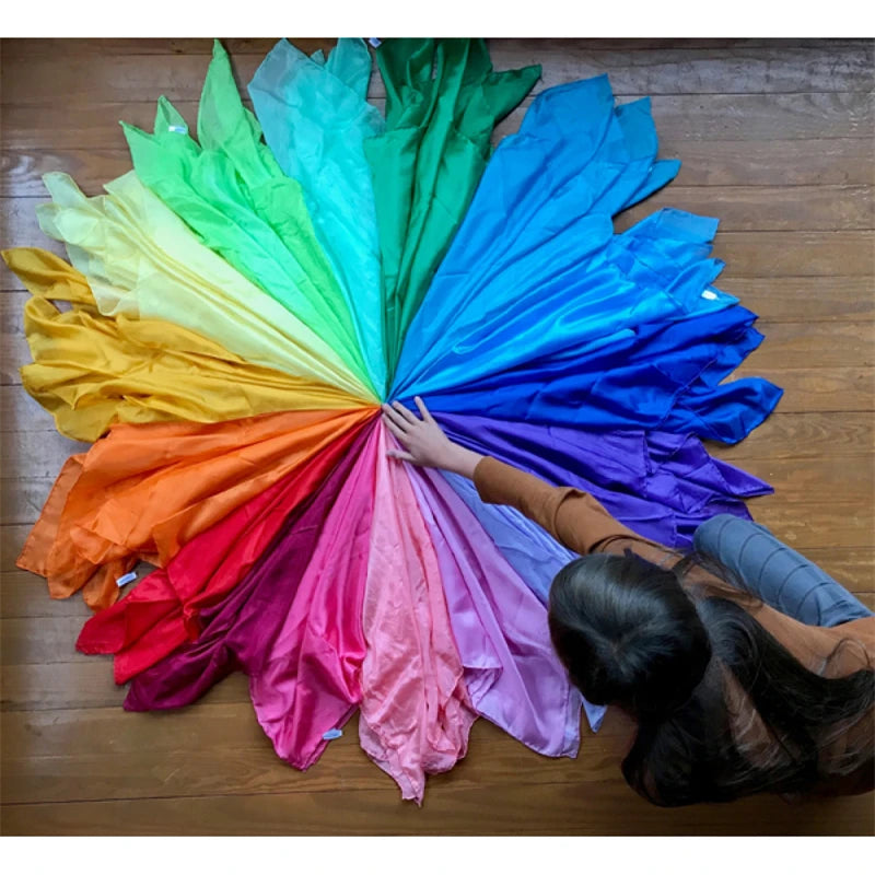 A fan of brightly colored Montessori Playsilks arranged in a vibrant rainbow spectrum.