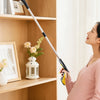 A pregnant woman holds a yellow foldable reacher grabber tool in a bright room next to wooden shelves.