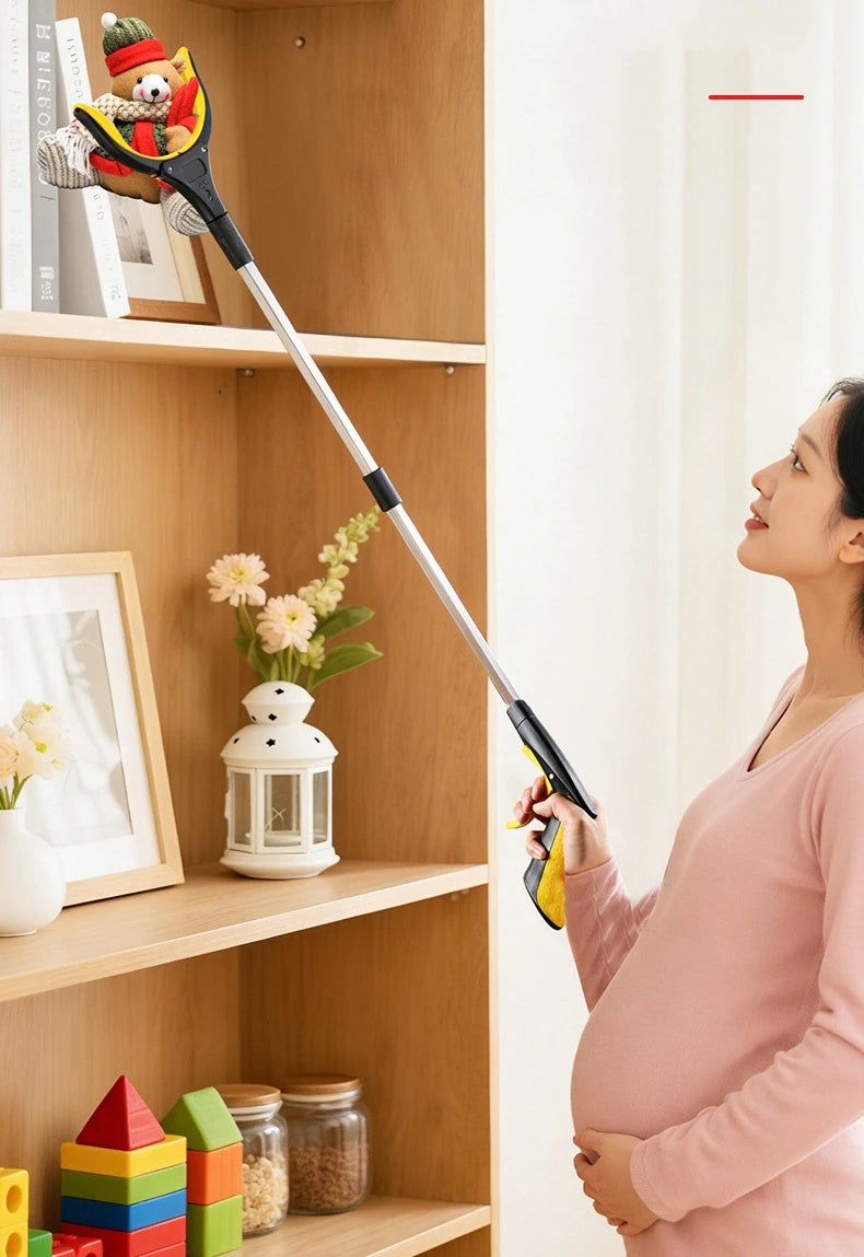 A pregnant woman holds a yellow foldable reacher grabber tool in a bright room next to wooden shelves.
