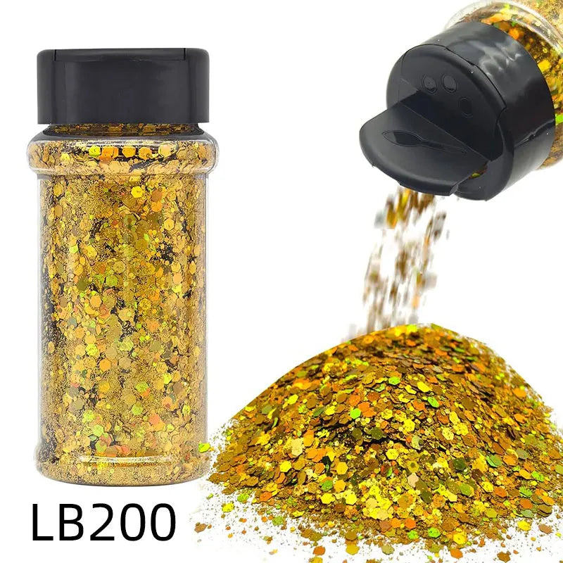 A glass jar of holographic chunky nail glitter mix with a black shaker top next to a pile of loose glitter.