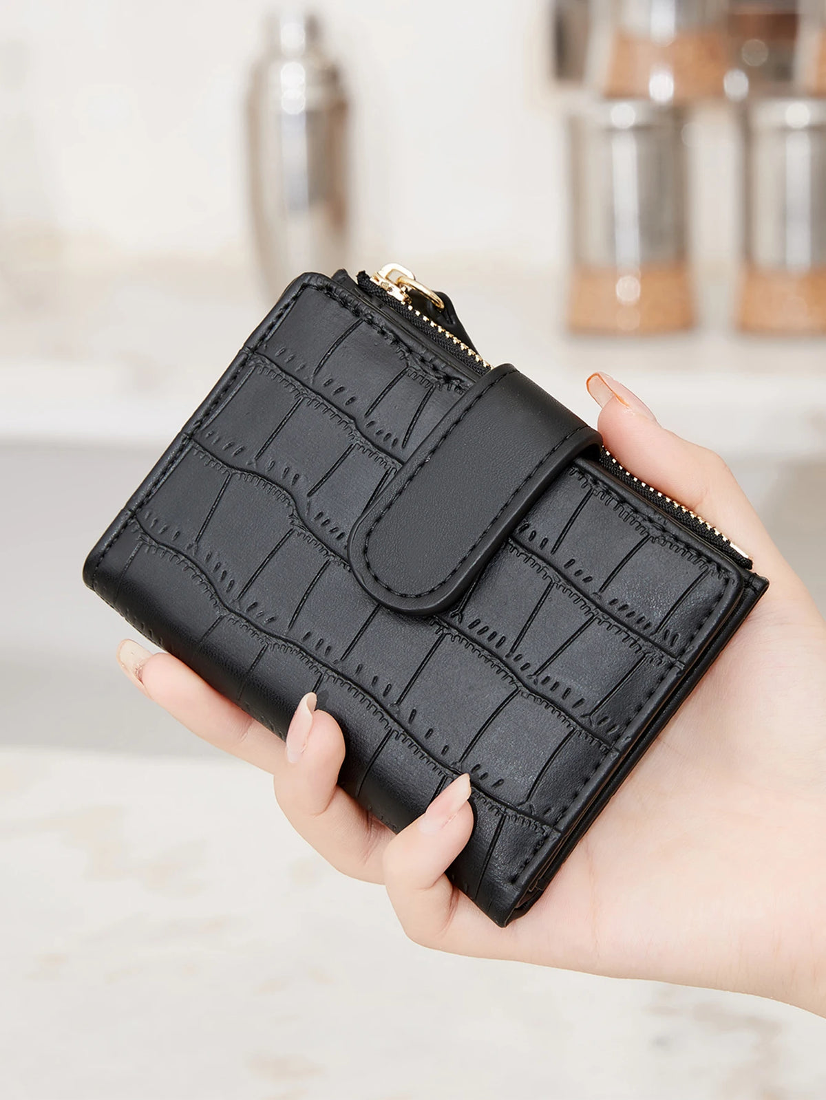 A hand holds a black quilted zippered wallet with card slots and coin pocket.