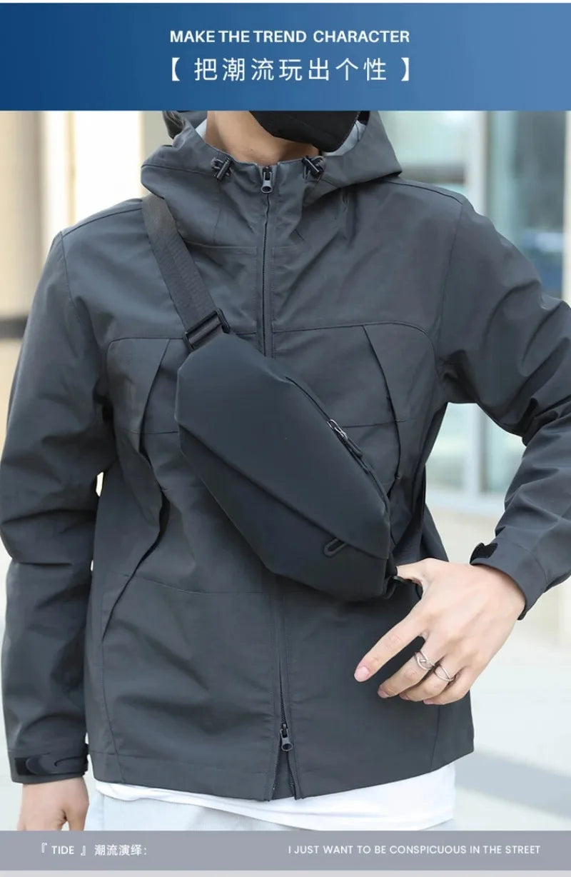 A man wearing a gray waterproof jacket with a black waist pack, posing outdoors.