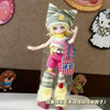 A female doll dressed in a sweet maid outfit featuring a striped hat, pink shorts, and yellow leg warmers.