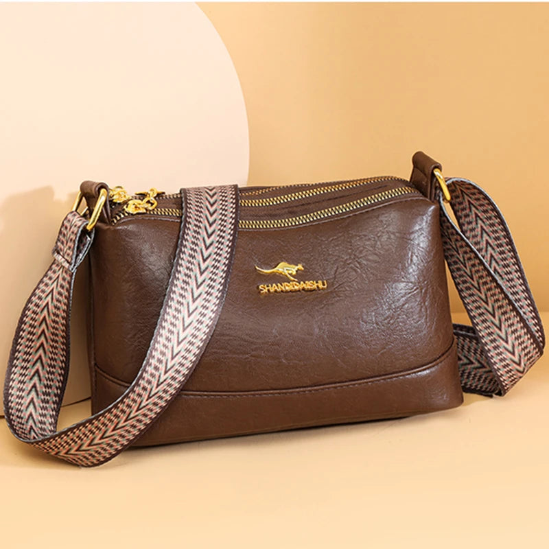 A brown PU leather crossbody shoulder bag with gold hardware and patterned strap resting on a light background.