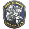 A dark blue embroidered patch featuring a silver archangel St. Michael with wings and a sword, surrounded by yellow text that