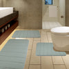 A set of light blue plush memory foam bath mats with non-slip backing placed on a tiled bathroom floor.
