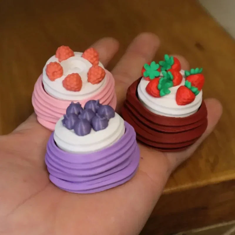 A hand holds three small cakes decorated with frosting and fruit, including orange, purple, and green elements.
