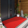 A red premium doormat placed on a gray tiled floor in front of a dark door.