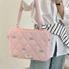 A pink quilted laptop shoulder bag with a bow detail is being held by a person wearing a white shirt and jeans.