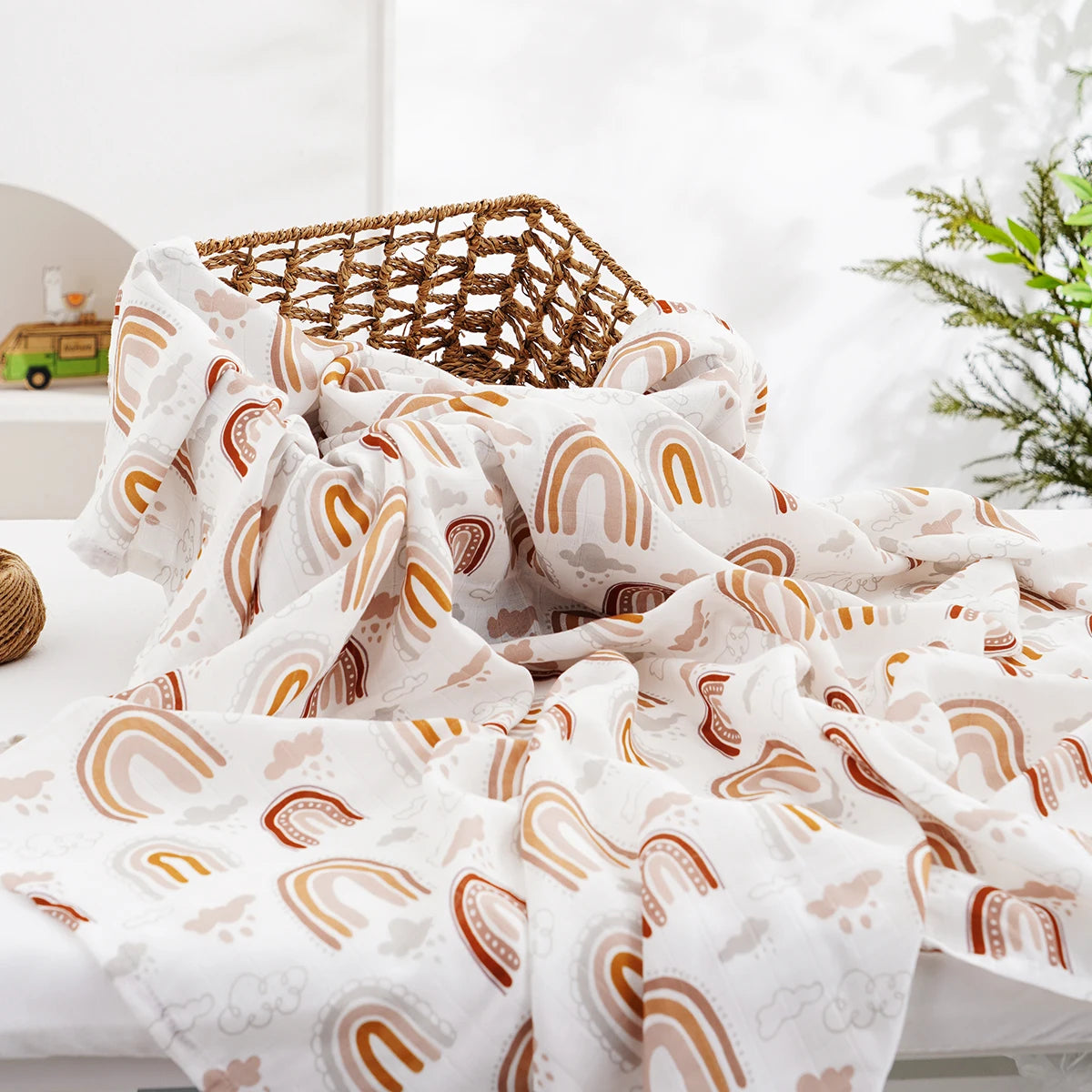 A white muslin baby swaddle blanket with a rainbow pattern is draped over a surface next to a woven basket.