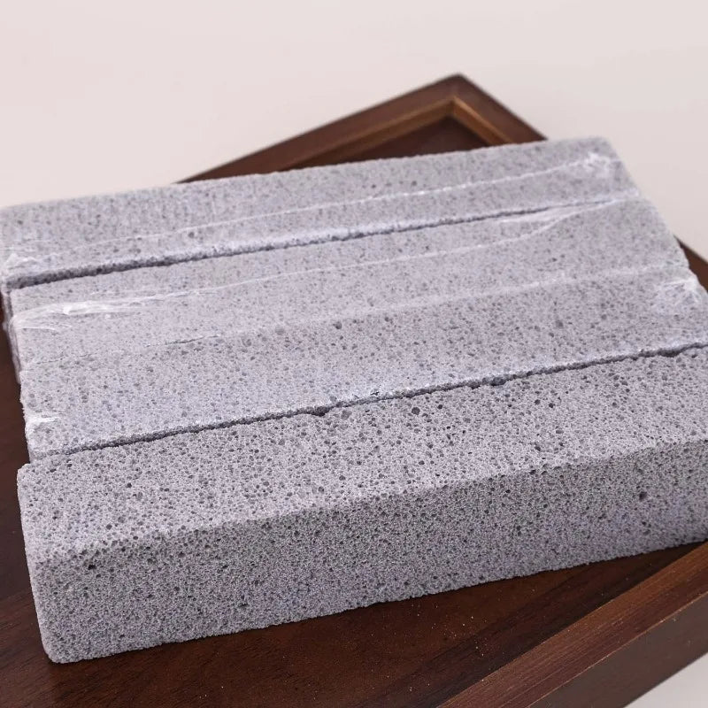 A stack of gray pumice stone cleaning sticks for stain removal placed on a wooden surface.
