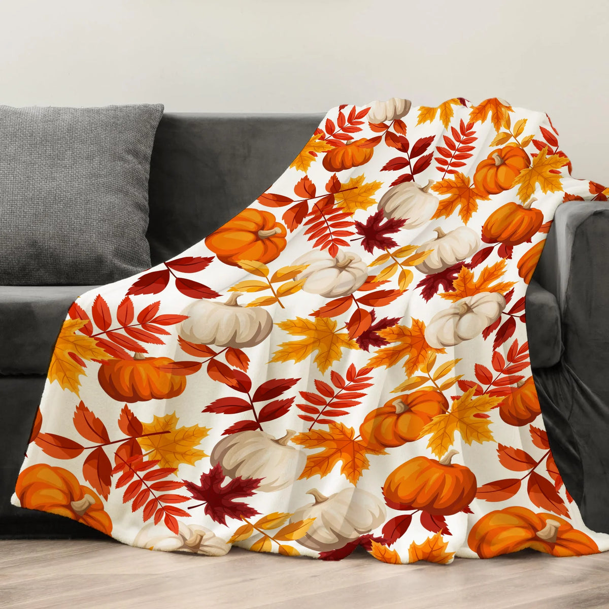 A colorful flannel throw blanket featuring an autumn pattern of orange and yellow maple leaves and pumpkins.