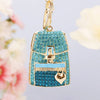 A gold-toned handbag keychain featuring bright turquoise blue crystal rhinestones and a silver zipper detail.