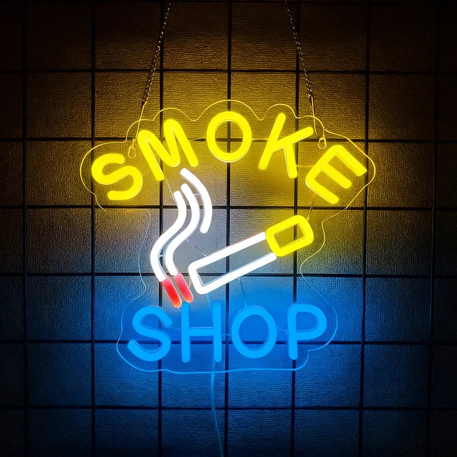 Neon sign shaped like a cloud with the words SMOKE SHOP glowing yellow and blue against a dark grid background