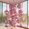 A collection of ten metallic pink round foil balloons are displayed hanging in front of a large window.