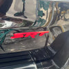 Close-up of a black car grille with a red SRT emblem and a green accent piece.