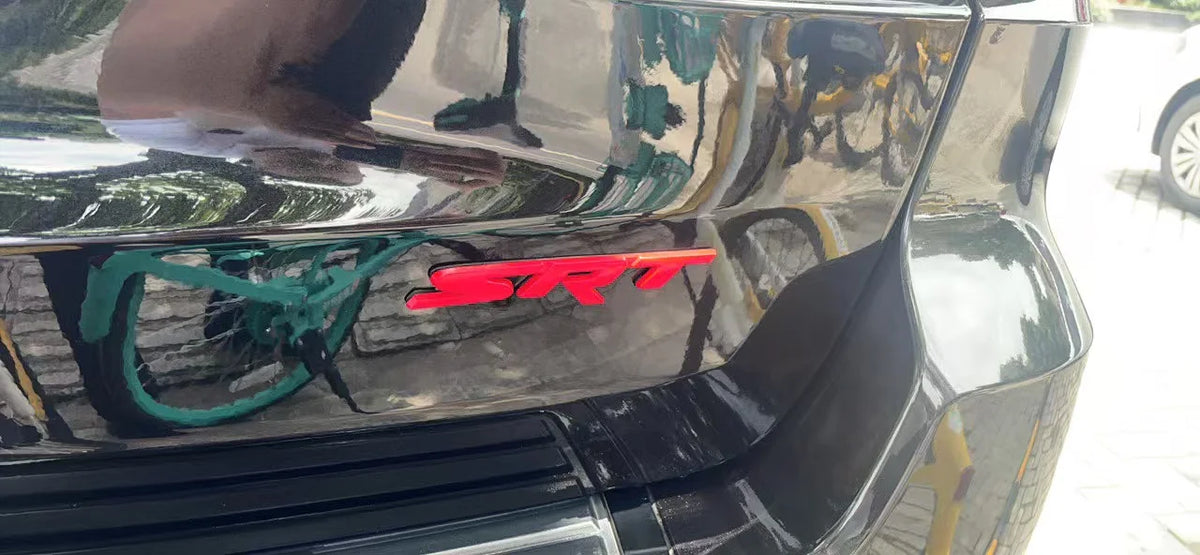 Close-up of a black car grille with a red SRT emblem and a green accent piece.