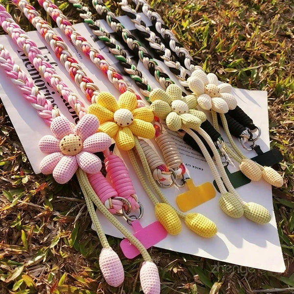 A display of various crossbody phone lanyards featuring decorative rope and pom-pom accents in pink, yellow, and black.