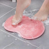 A pink silicone shower mat with exfoliating bristles is placed on a gray tiled floor, showing wet feet.