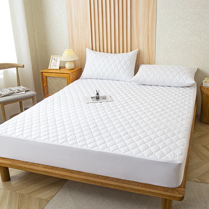 A white fitted mattress protector is displayed on a wooden bed frame with a quilted surface.