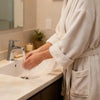 A person is using a touchless automatic soap dispenser at a kitchen sink with a white ceramic basin.