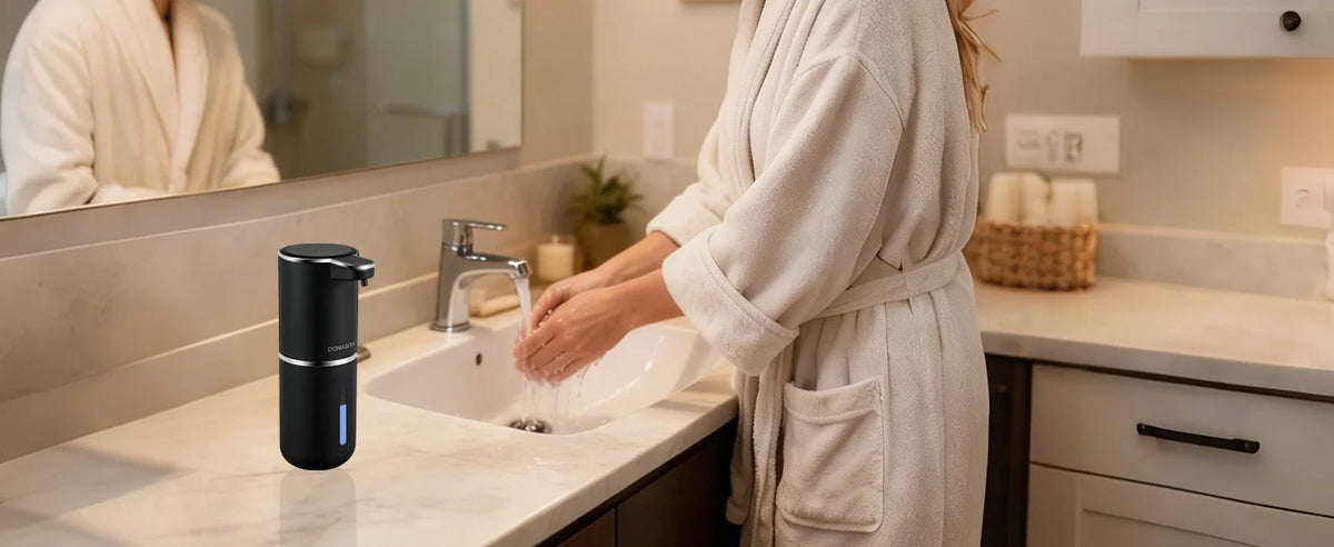 A person is using a touchless automatic soap dispenser at a kitchen sink with a white ceramic basin.