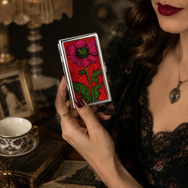 A hand holds a vintage snap card holder featuring a vibrant pink and green floral design against a dark background.