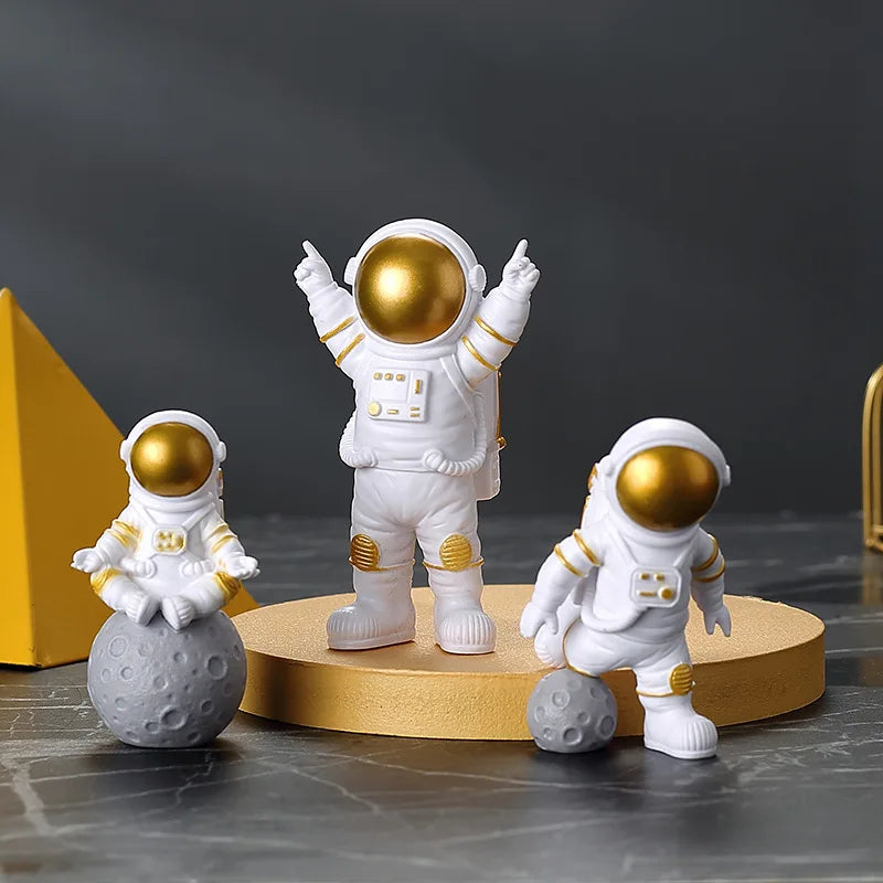 A set of three handcrafted white astronaut figurines with gold helmets standing on a yellow circular base.