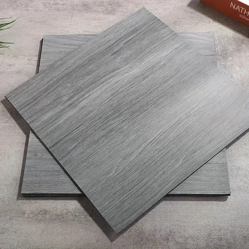 A stack of gray wood grain peel and stick vinyl flooring tiles displayed on a light surface.