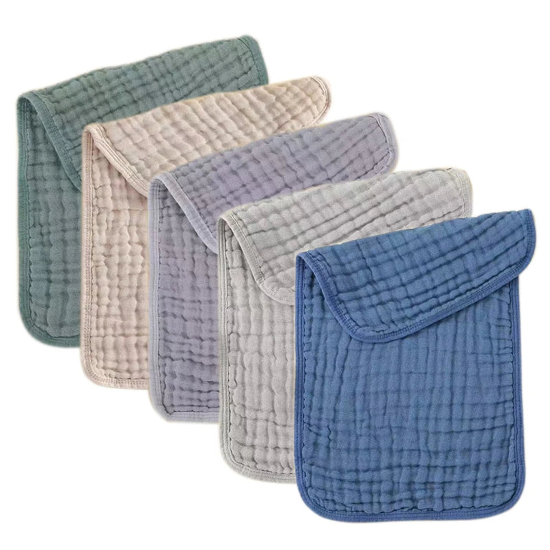 A stack of five colored muslin baby burp cloths in shades of green, beige, purple, gray, and blue.