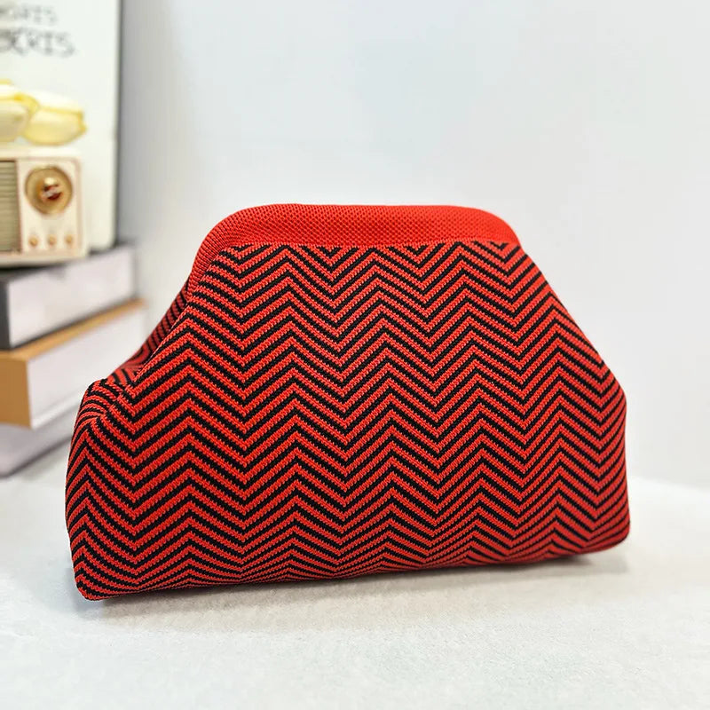 Clutch de chevron rojo y negro tejido con tapa lisa, sobre una superficie blanca.