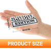 Eine Hand hält ein Set aus 3D-Aufklebern (Decals) der Shitbox Edition in Schwarz und Weiß für das Auto.