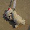 A white, fluffy plush toy resembling a bear with pink accents is hanging against a beige wall.