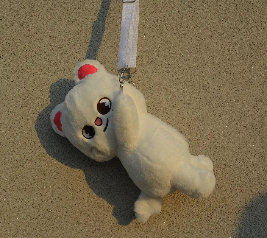 A white, fluffy plush toy resembling a bear with pink accents is hanging against a beige wall.