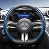 Close-up view of a black steering wheel with blue carbon fiber texture accents and a Mercedes-Benz emblem.