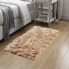 A fluffy, light brown faux fur area rug placed on a wooden floor next to a white bed and a decorative shelf.